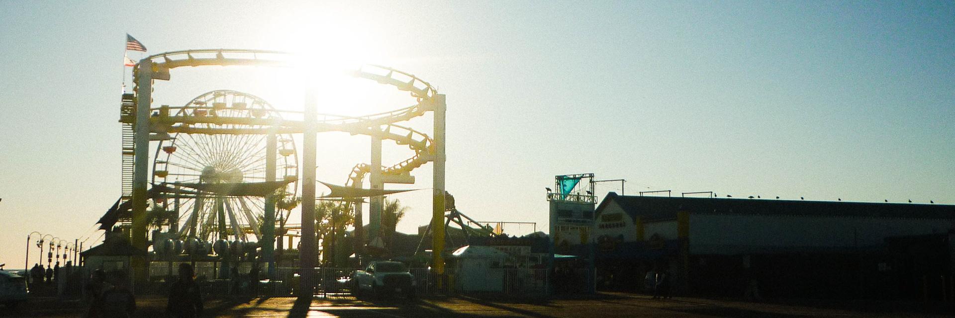 A Ferris wheel and roller coaster backlit by the sun.